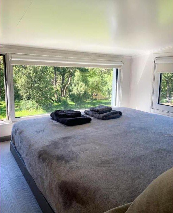 Cama doble en el entrepiso con ventanal al jardín