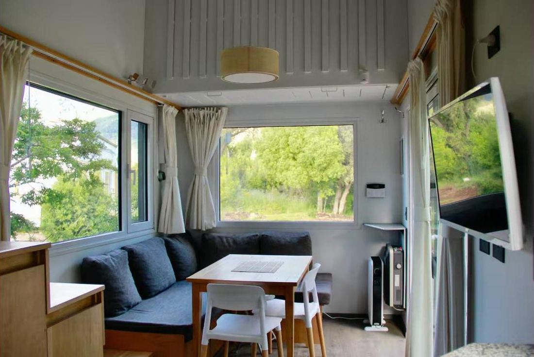 Living con sillón en L, mesa y ventanales al bosque